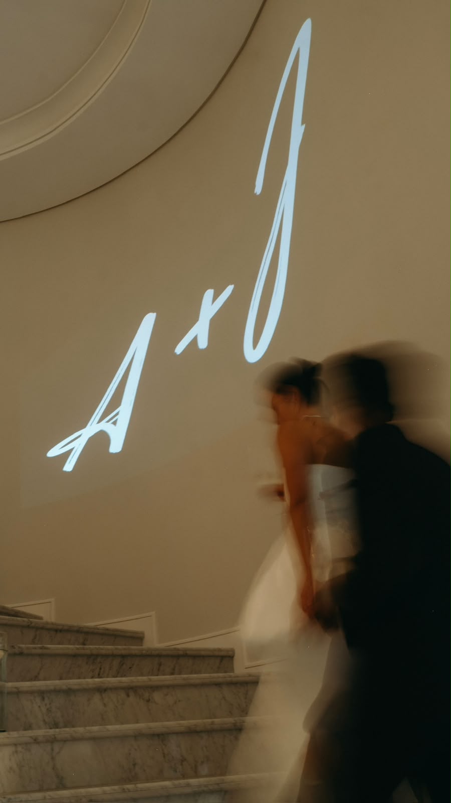 Couple walking up a marble staircase under projected initials